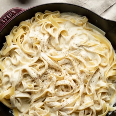 square image of fettuccine alfredo with black pepper in cast iron pan