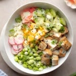 square image of tofu poke bowl with cucumbers, edamame and mango on beige background