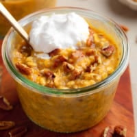 close up on a glass jar of pumpkin overnight oats topped with pecans and whipped cream.