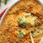 a spoon lifting a scoop of vegan broccoli casserole from a large casserole dish.