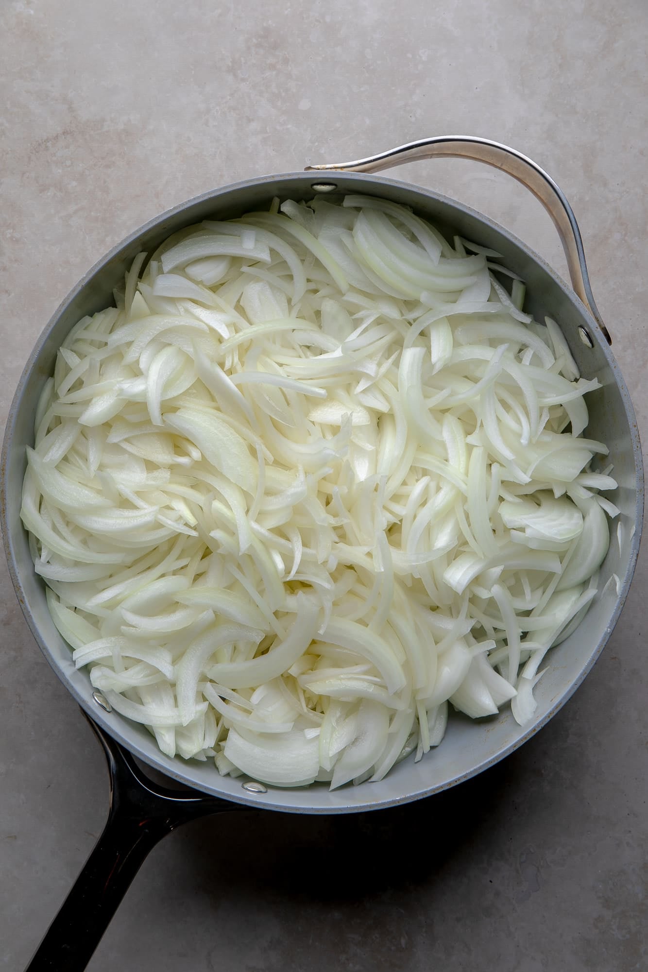 overhead view of raw sliced onions in a large skillet.
