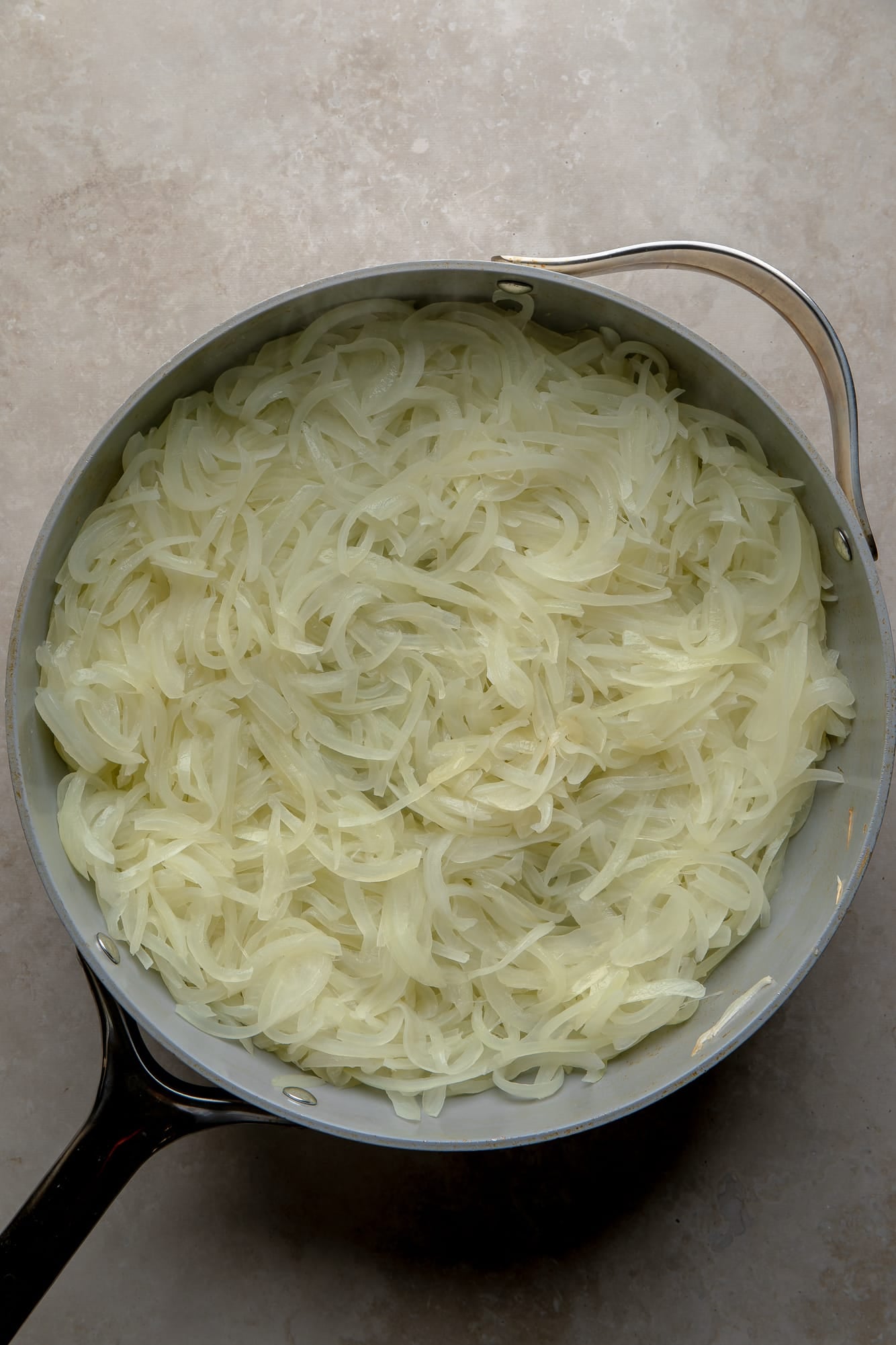 overhead view of sliced onions cooking in a large skillet.
