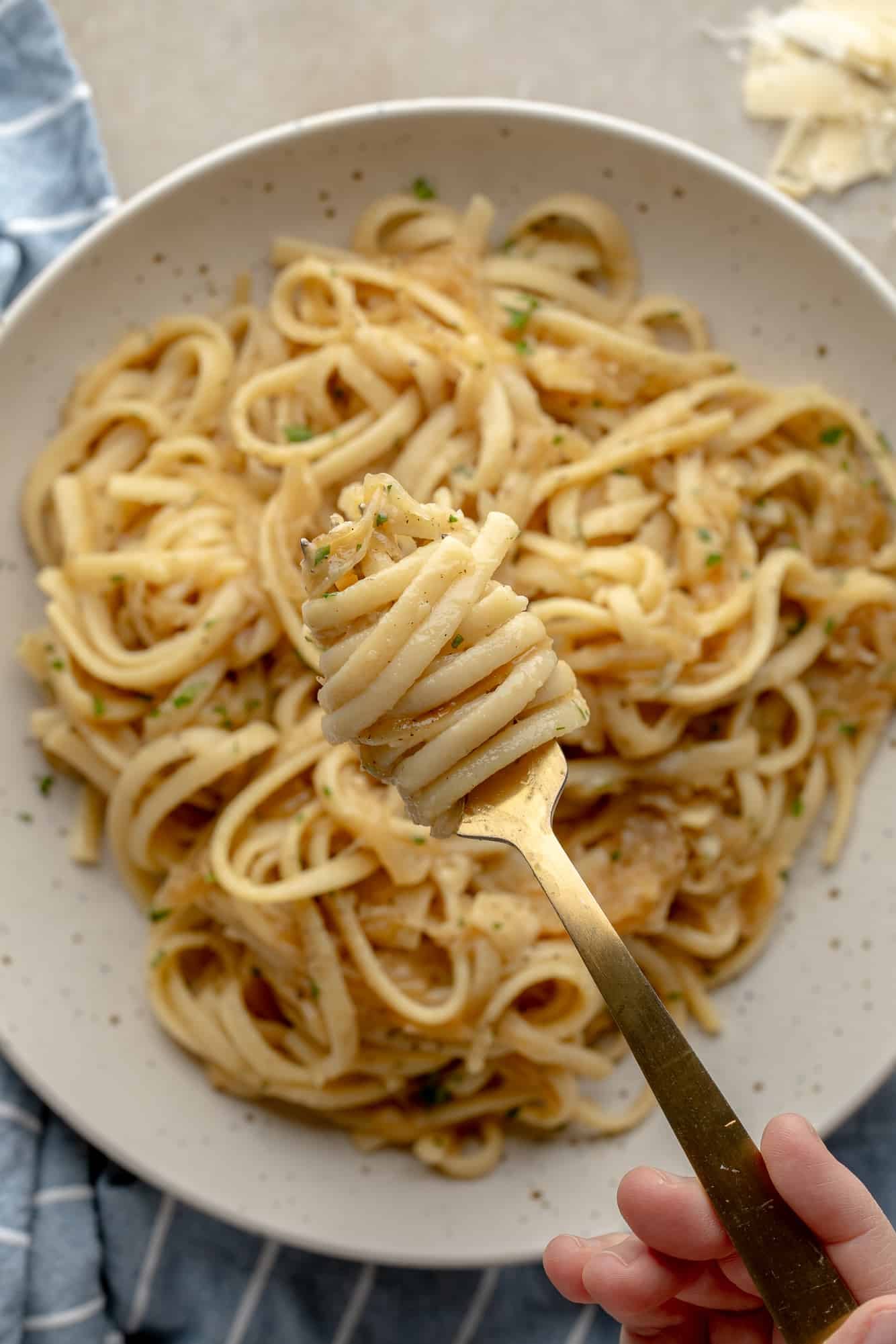 close up on a fork holding a bite of vegan caramelized onion pasta above a bowl with more pasta.