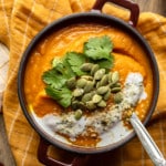 overhead view of a bowl of vegan carrot and ginger soup topped with cilantro and pepitas.
