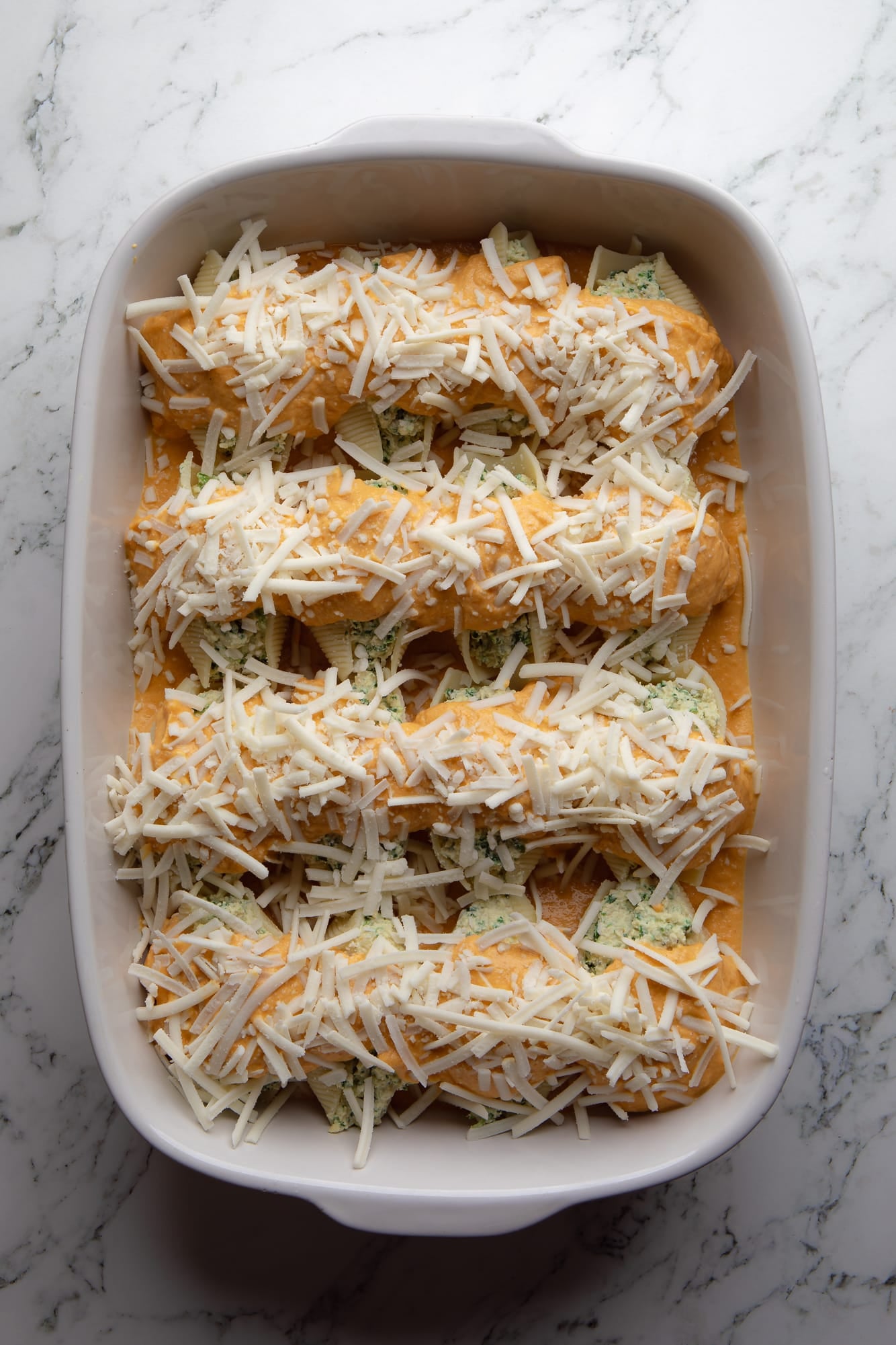 overhead view of vegan pumpkin stuffed shells covered in pumpkin sauce and vegan shredded cheese in a casserole dish.