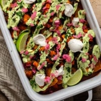 overhead view of sweet potato black bean enchiladas topped with avocado crema, vegan sour cream, pickled red onions, and lime wedges.