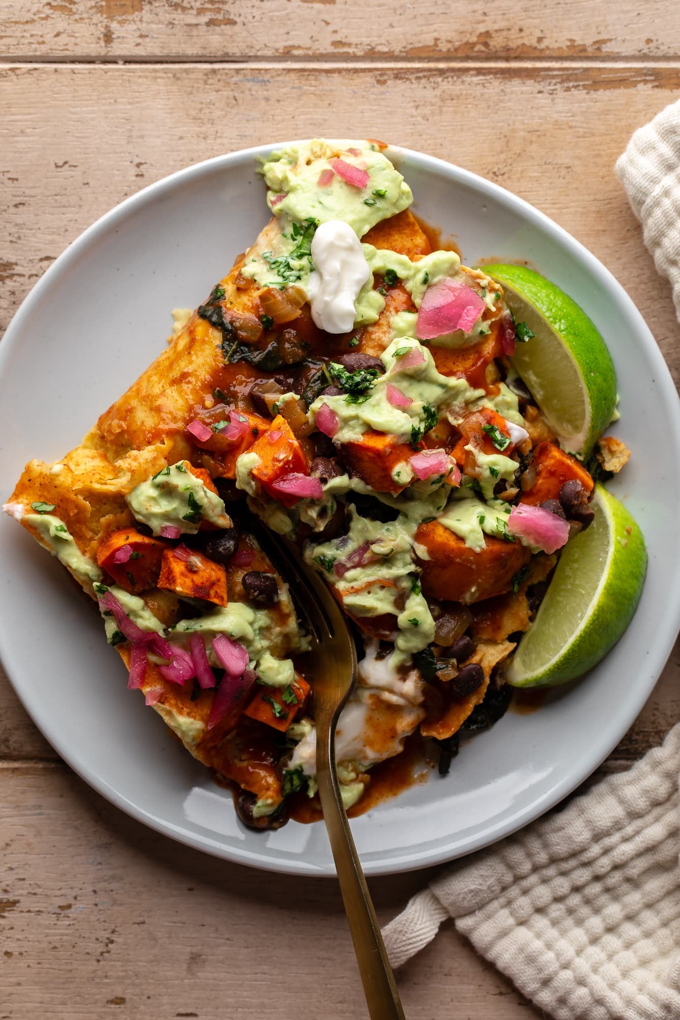 using a fork to cut into sweet potato black bean enchiladas on a plate.