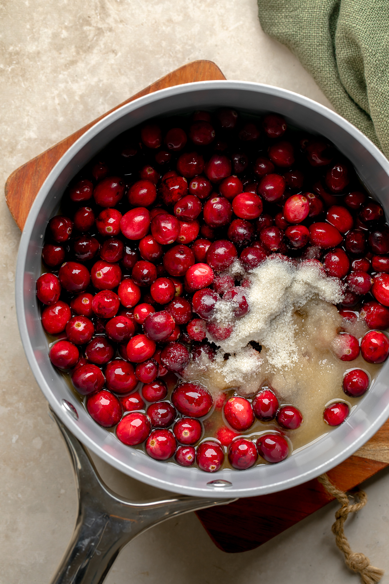 overhead view of fresh cranberries, sugar, and orange juice for orange cranberry sauce in a saucepan.