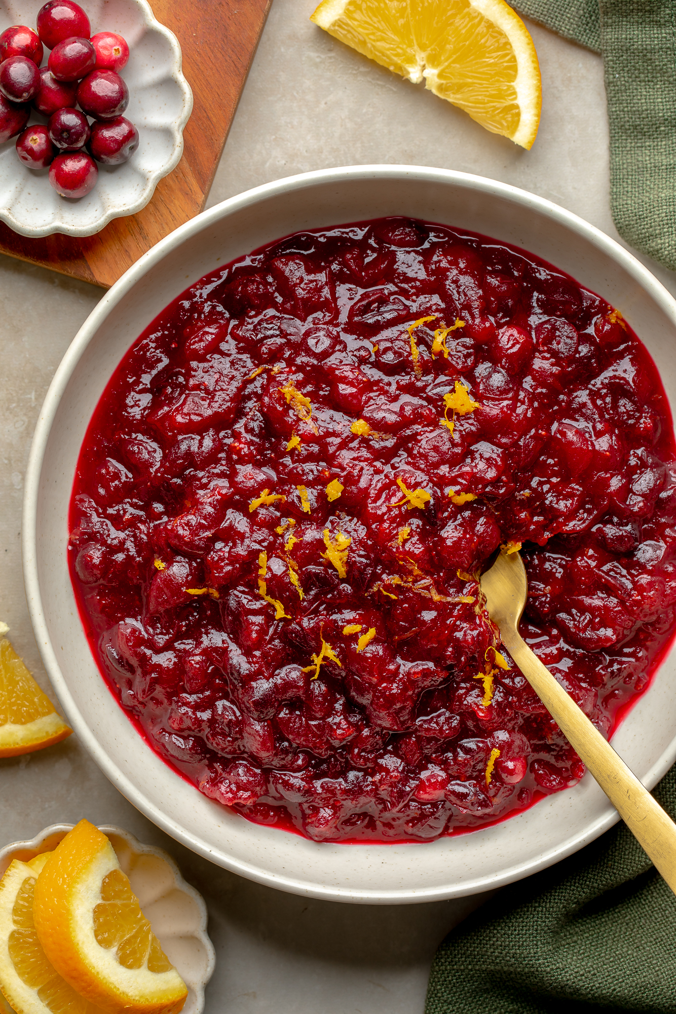 Overhead view of a bowl of orange cranberry sauce topped with orange zest with orange slices and fresh cranberries on the side.