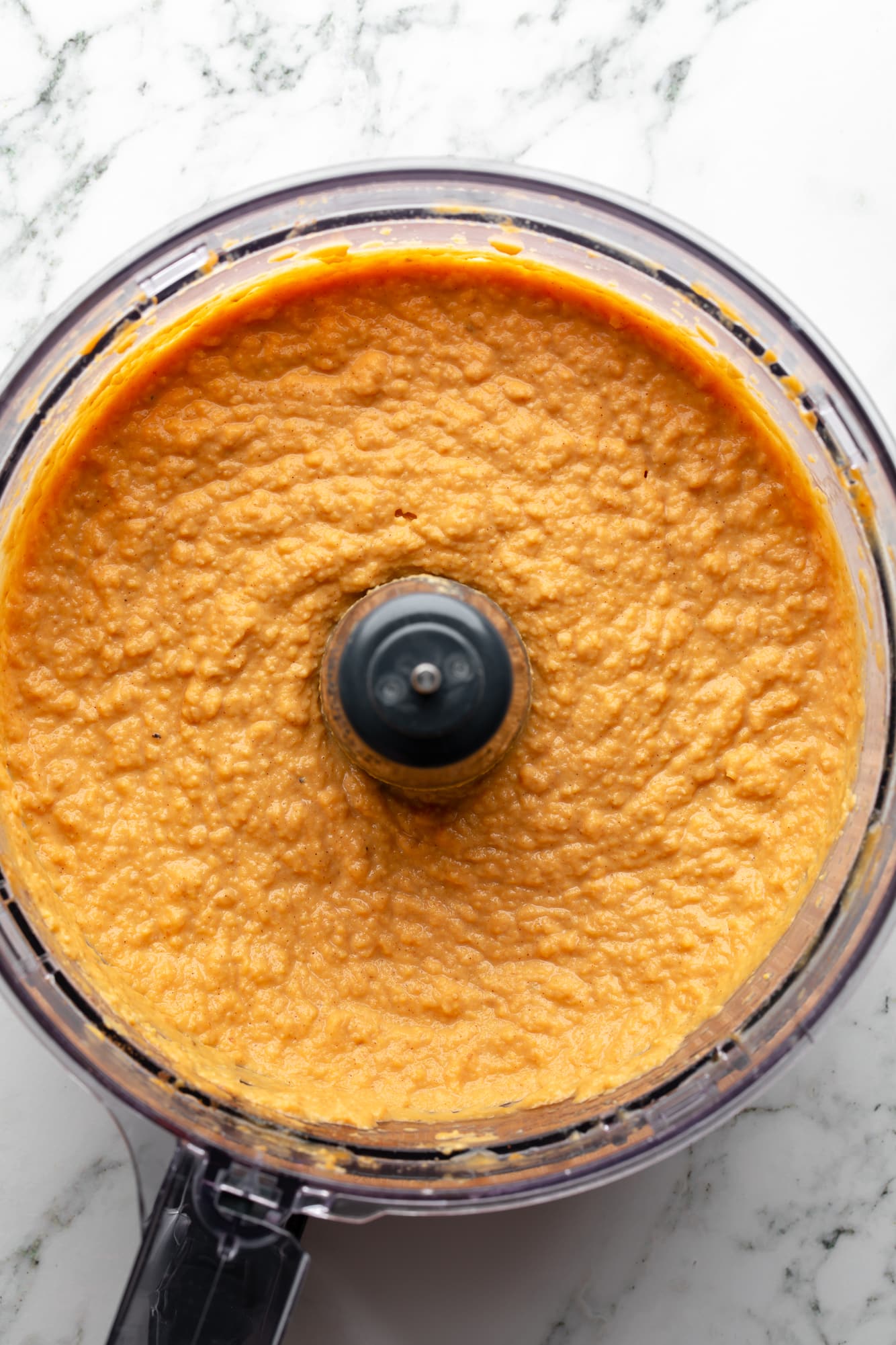 overhead view of a bowl of orange pumpkin hummus in a food processor.