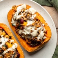 close up on two stuffed butternut squashes topped with garlic tahini sauce on a white plate.