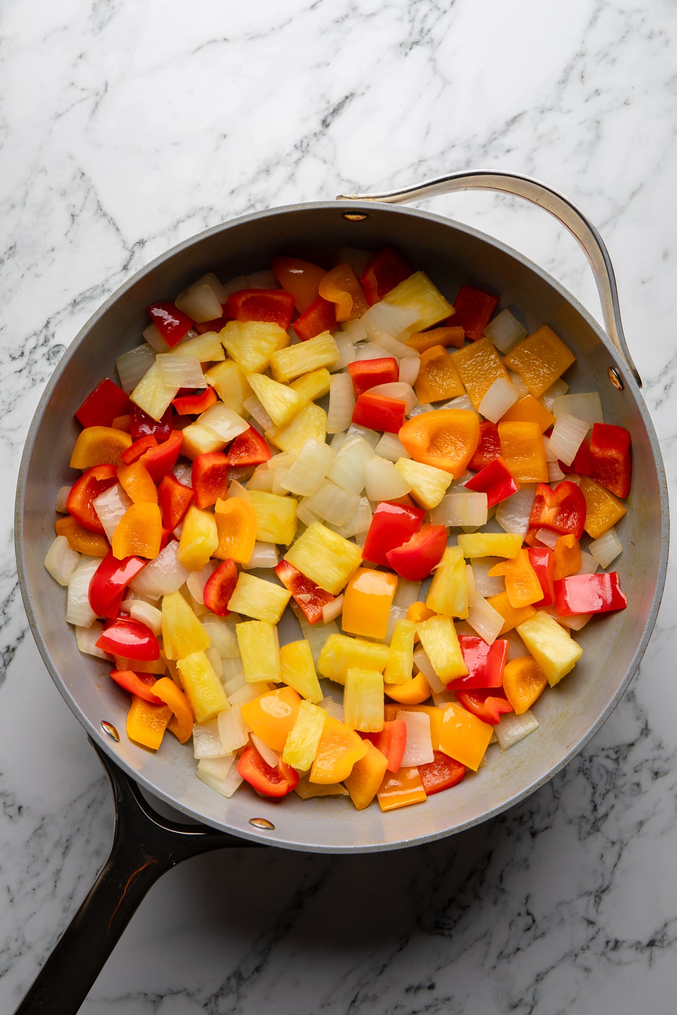 overhead view of chopped and cooked bell peppers and onions in a skillet.