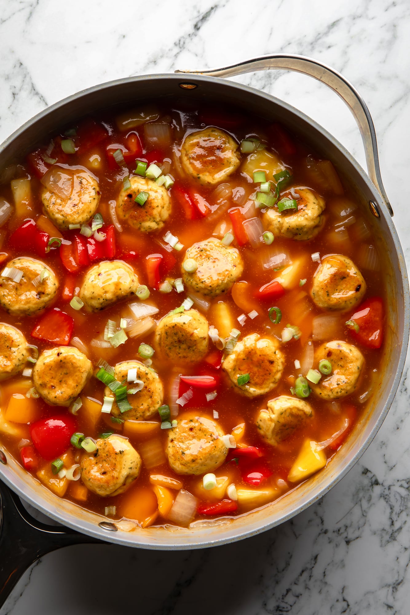simmering tofu meatballs and vegetables in red sweet and sour sauce in a large skillet.