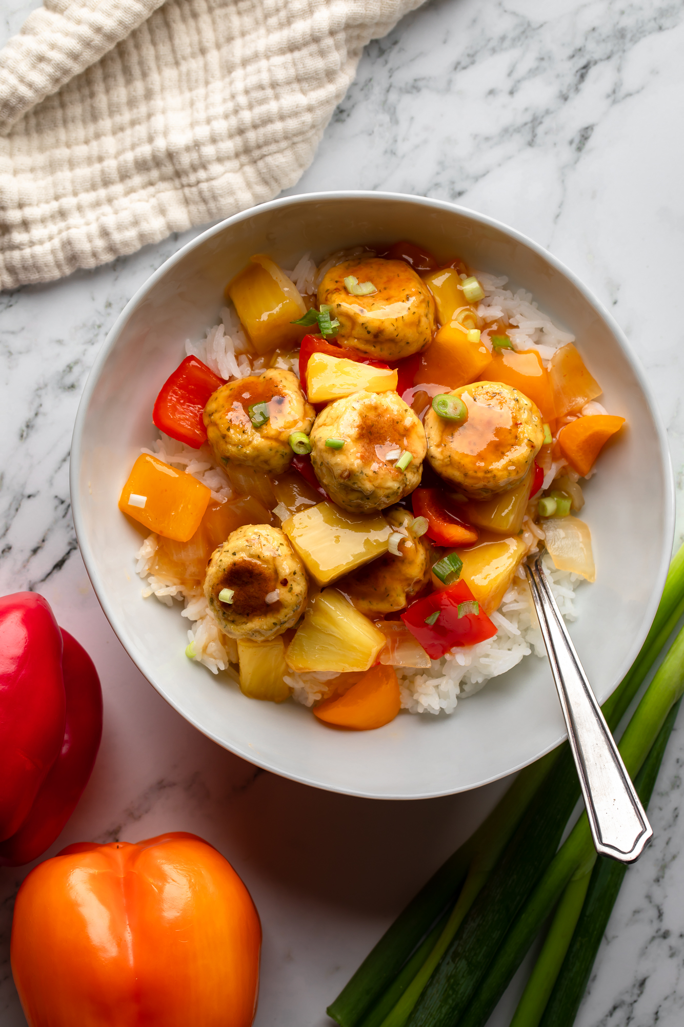 overhead view of sweet and sour tofu meatballs and vegetables over white rice in a white bowl.