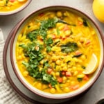 overhead view of a bowl of Golden Orzo Soup with Chickpeas topped with a lemon wedge, green herbs, and nuts.