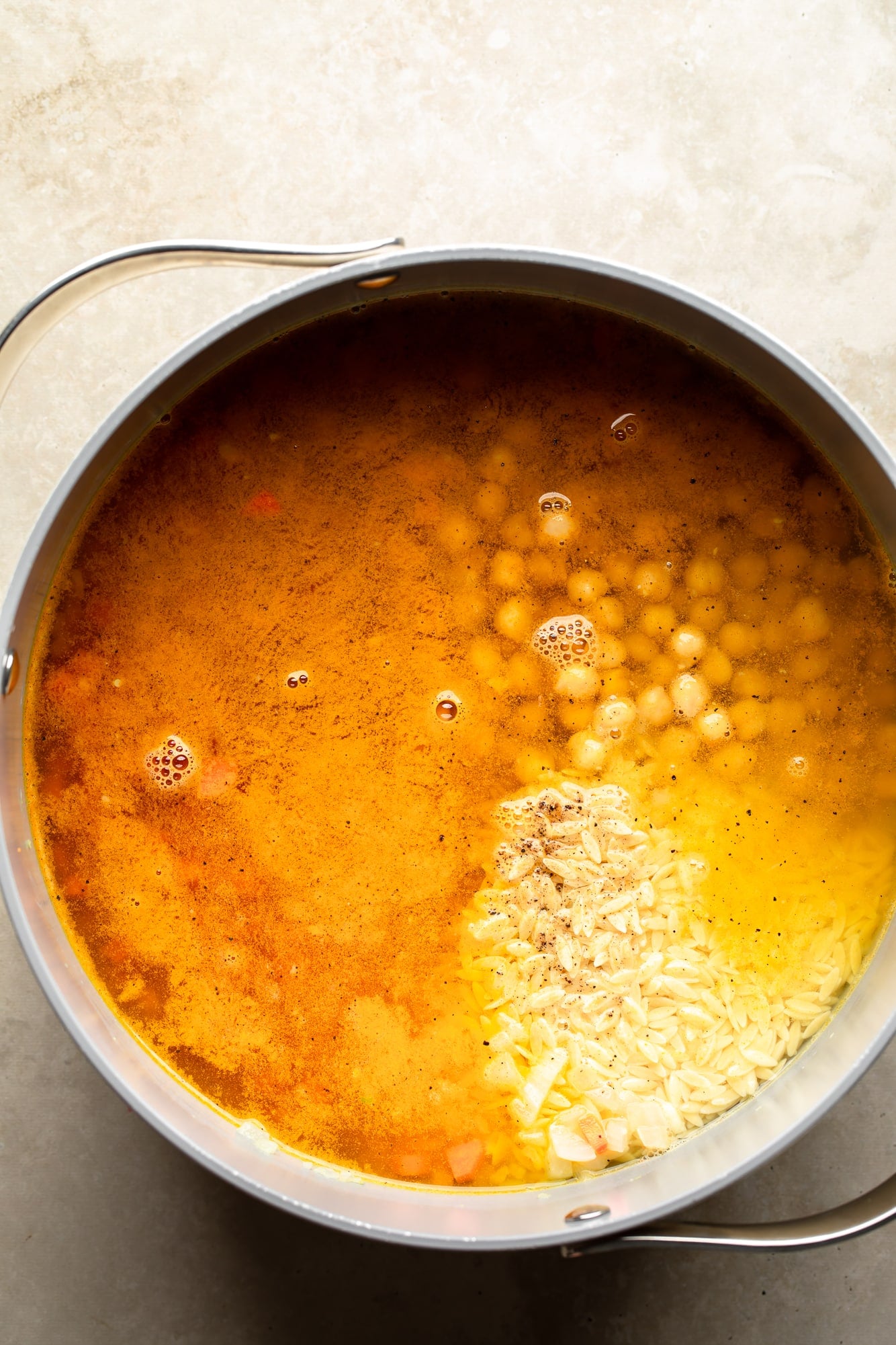 overhead view of the ingredients for Golden Orzo Soup with Chickpeas in a large pot.