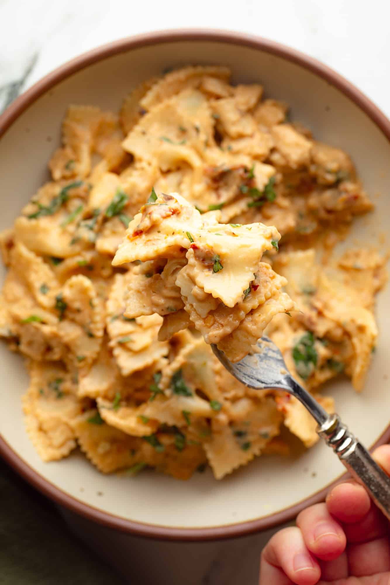 close up on a forkful of vegan marry me pasta being held above a bowl of pasta.