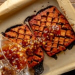 overhead view of a pineapple glaze being poured over a tofu ham roast in a parchment-lined baking dish.