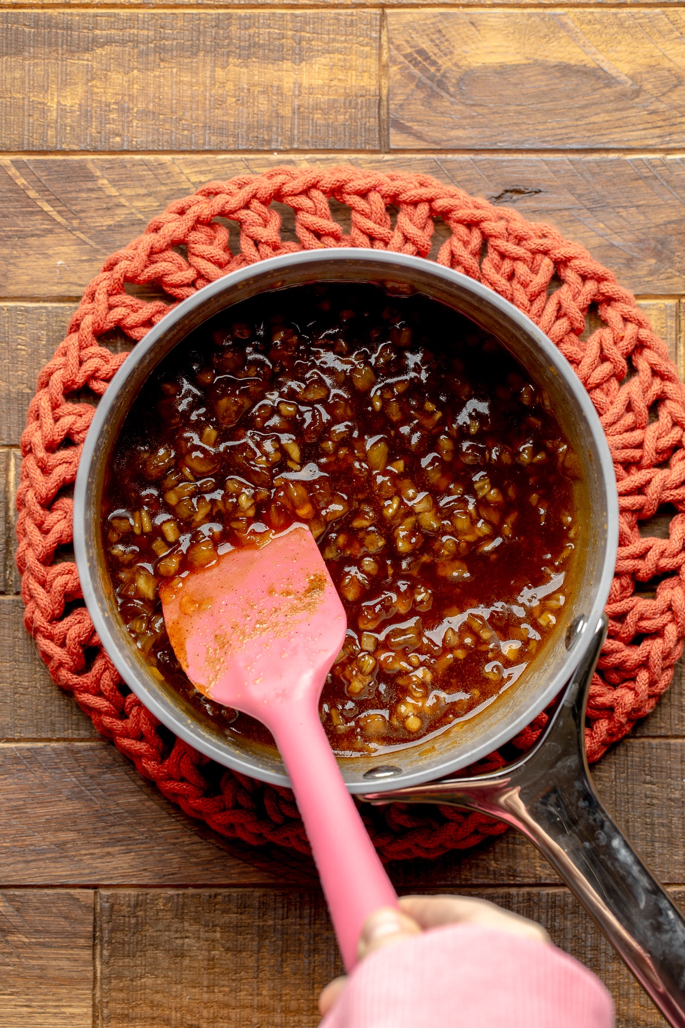 overhead view of a pink spatula stirring a pineapple glaze in a saucepan.