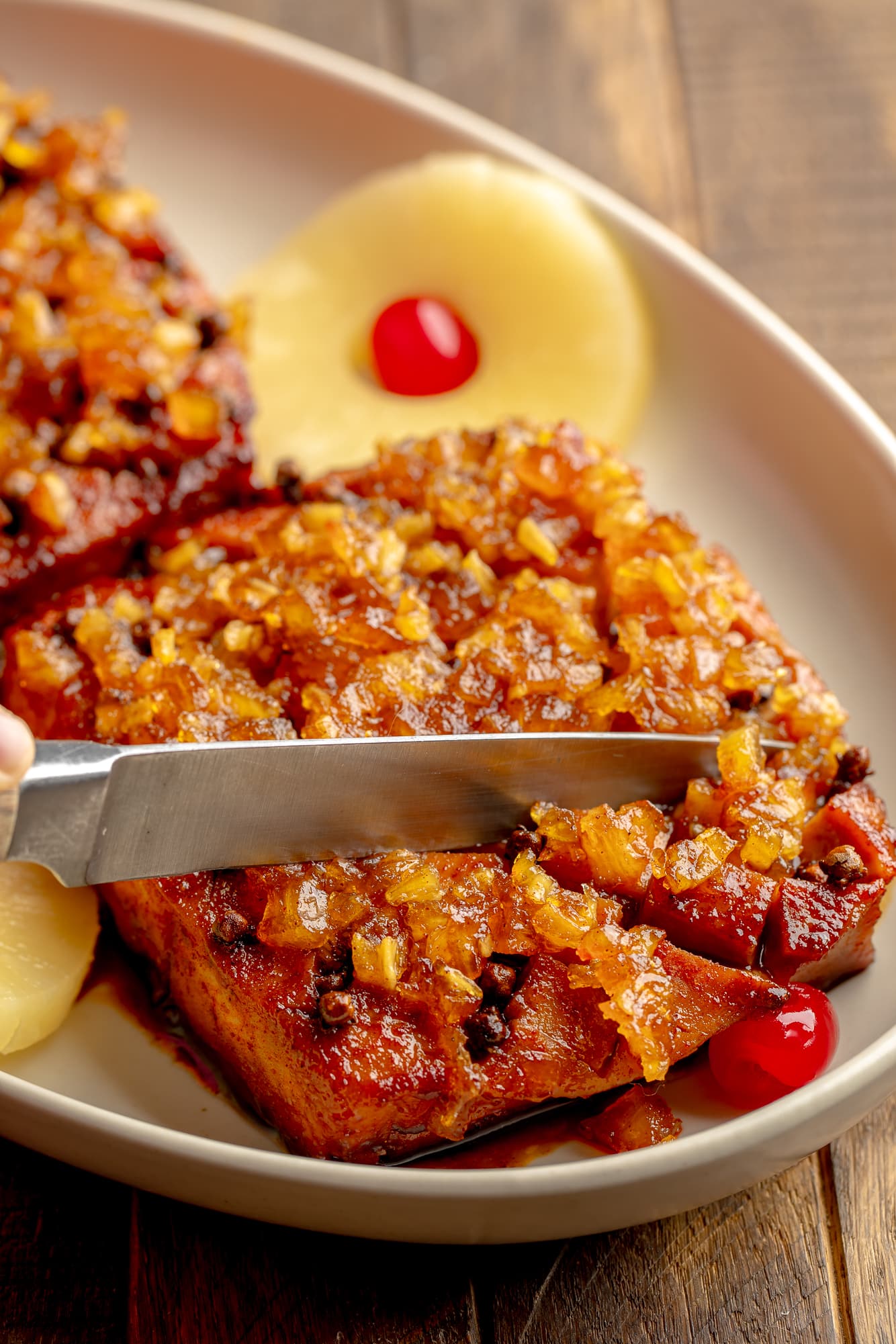 side view of a knife slicing into a pineapple glazed tofu roast in a serving dish.