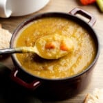 side view of a spoon being lifted out of a bowl of vegan split pea soup.