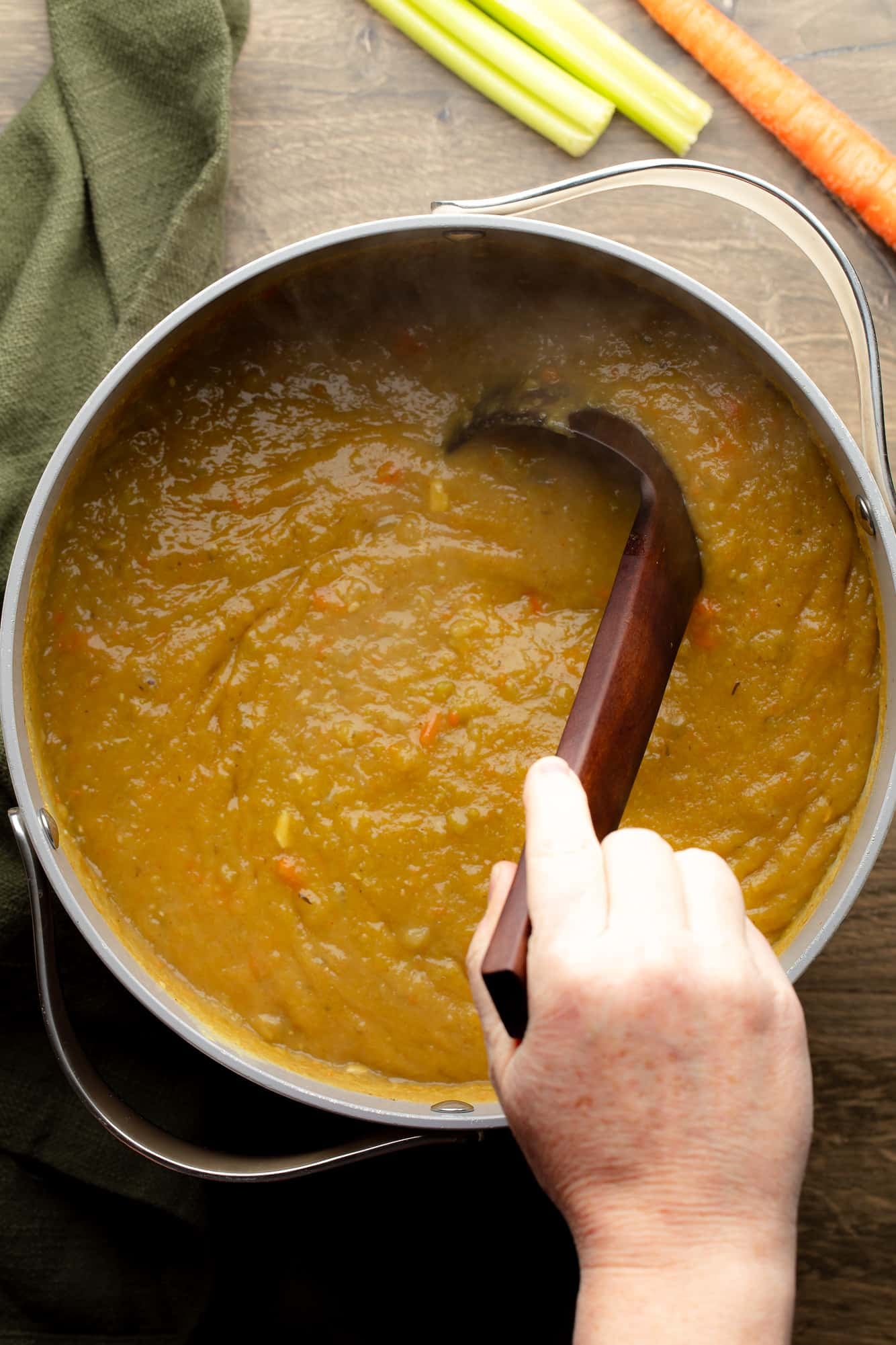 overhead view of a hand stirring a pot of vegan split pea soup with a ladle.