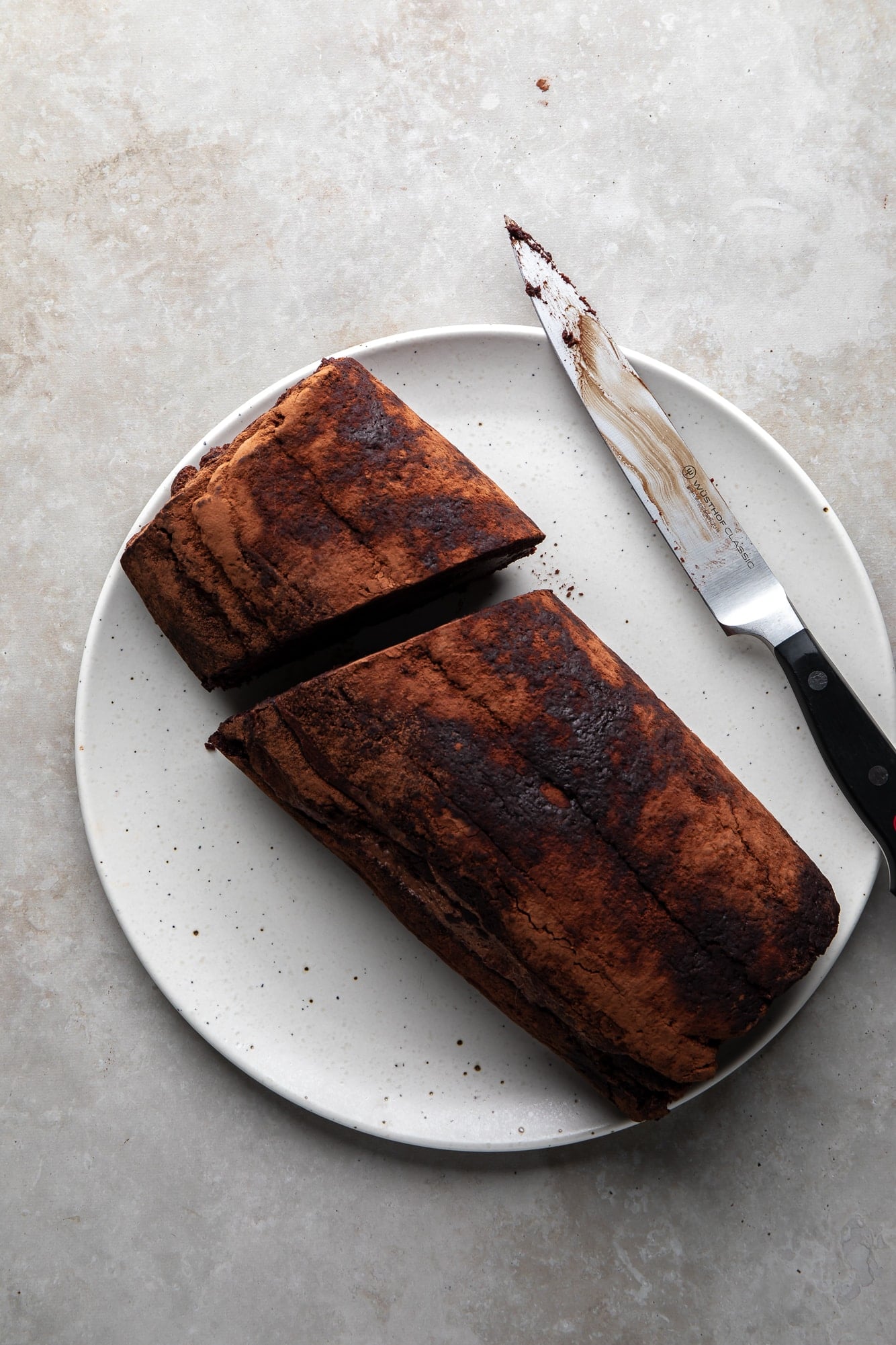 overhead view of a rolled yule log sliced in half next to a knife on a white plate.