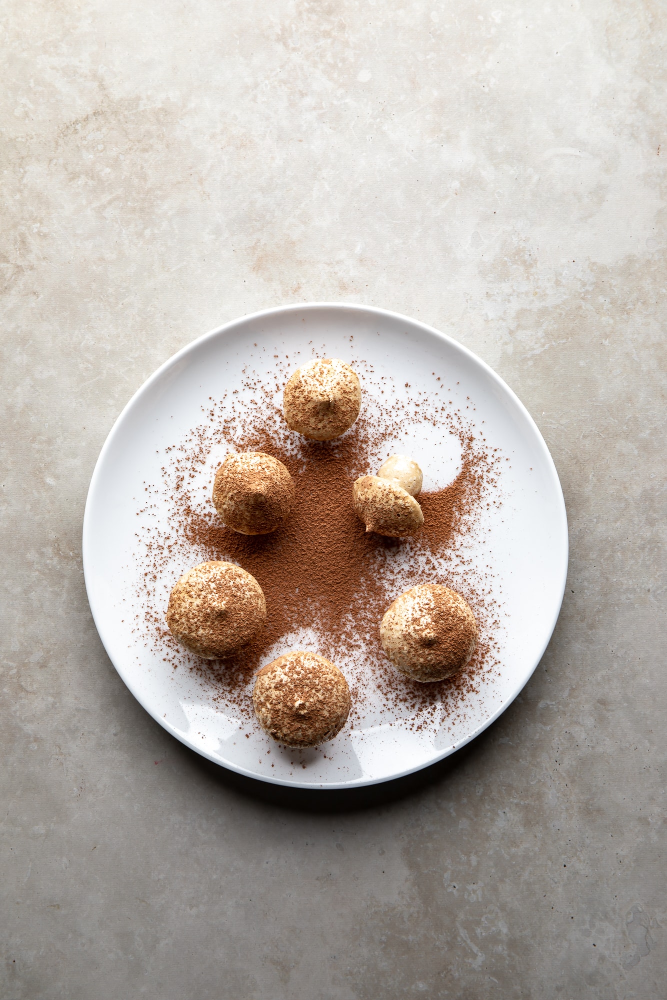 overhead view of vegan meringue mushrooms dusted with cocoa powder on a white plate.