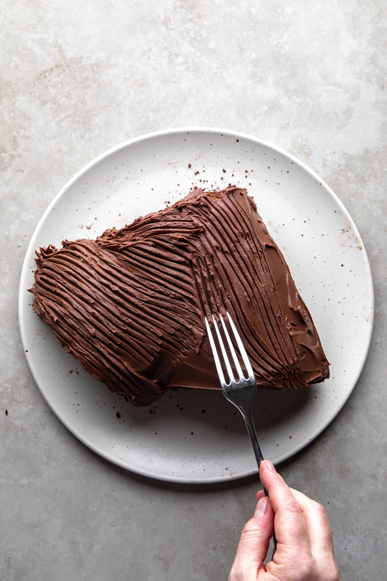 overhead view of a womans hand dragging a fork over a frosted yule log cake on a white plate.