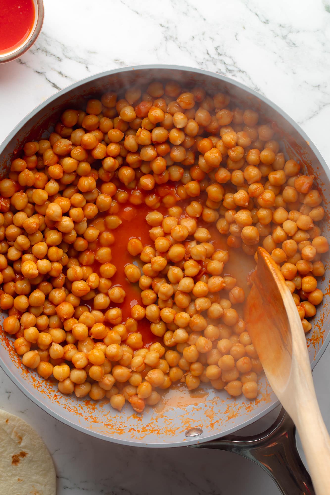 overhead view of a wooden spoon stirring buffalo chickpeas for buffalo chickpea tacos in a skillet.