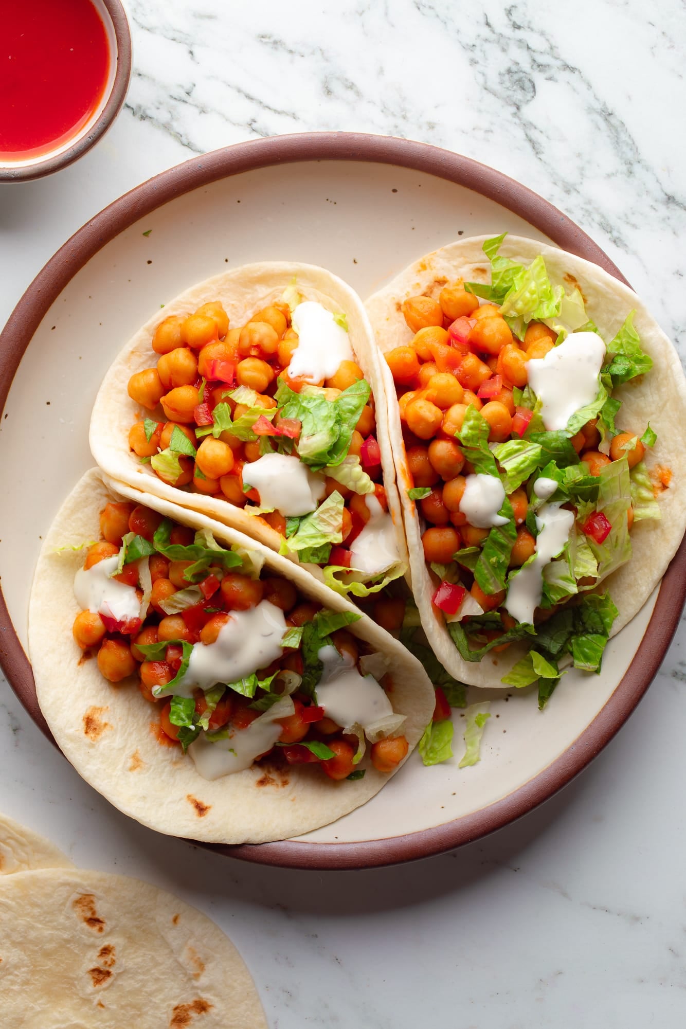 overhead view of 3 buffalo chickpea tacos topped with lettuce and vegan ranch on a plate.
