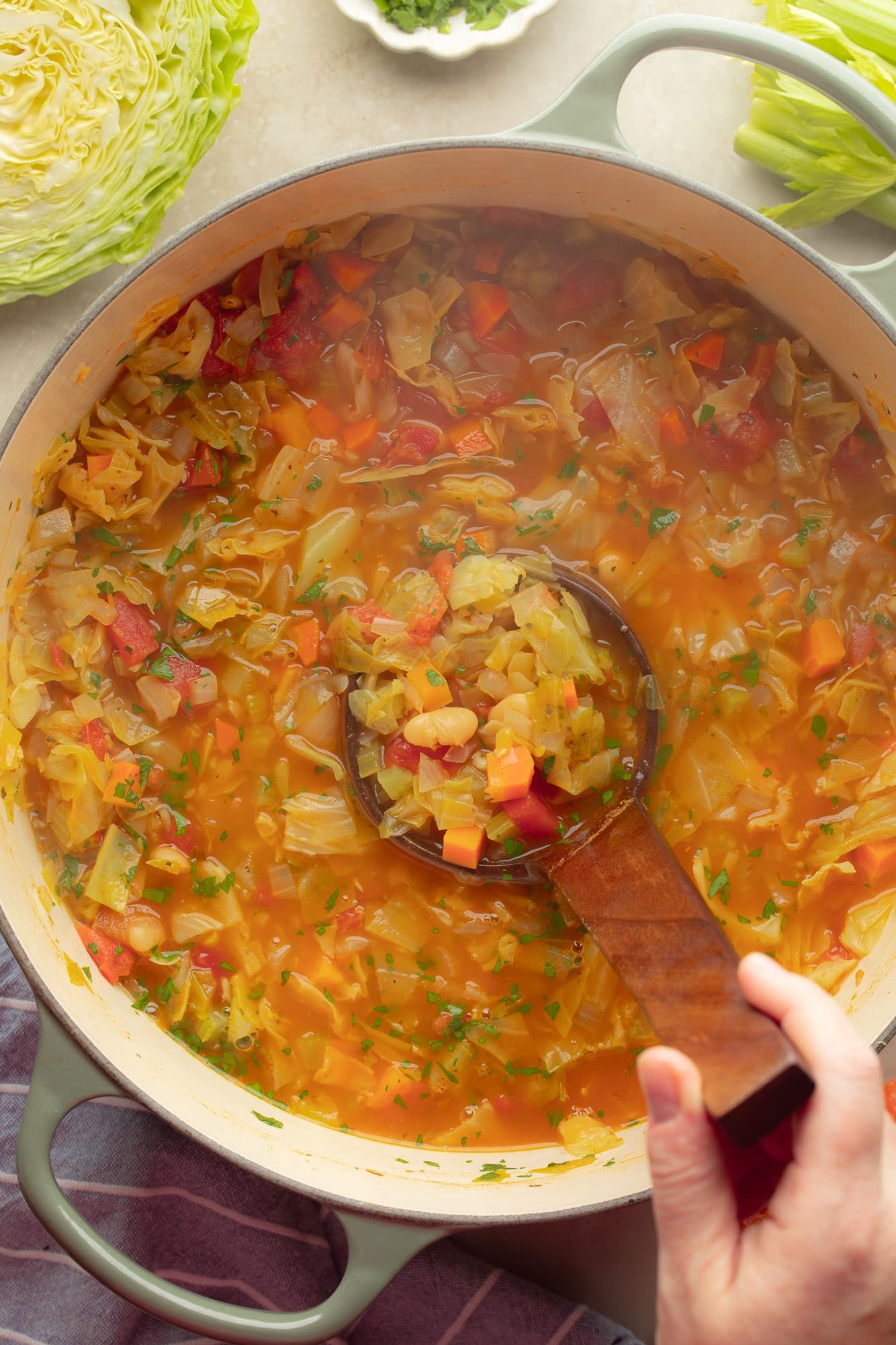 overhead view of a persons hand lifting a ladle out of a pot of vegan cabbage soup.