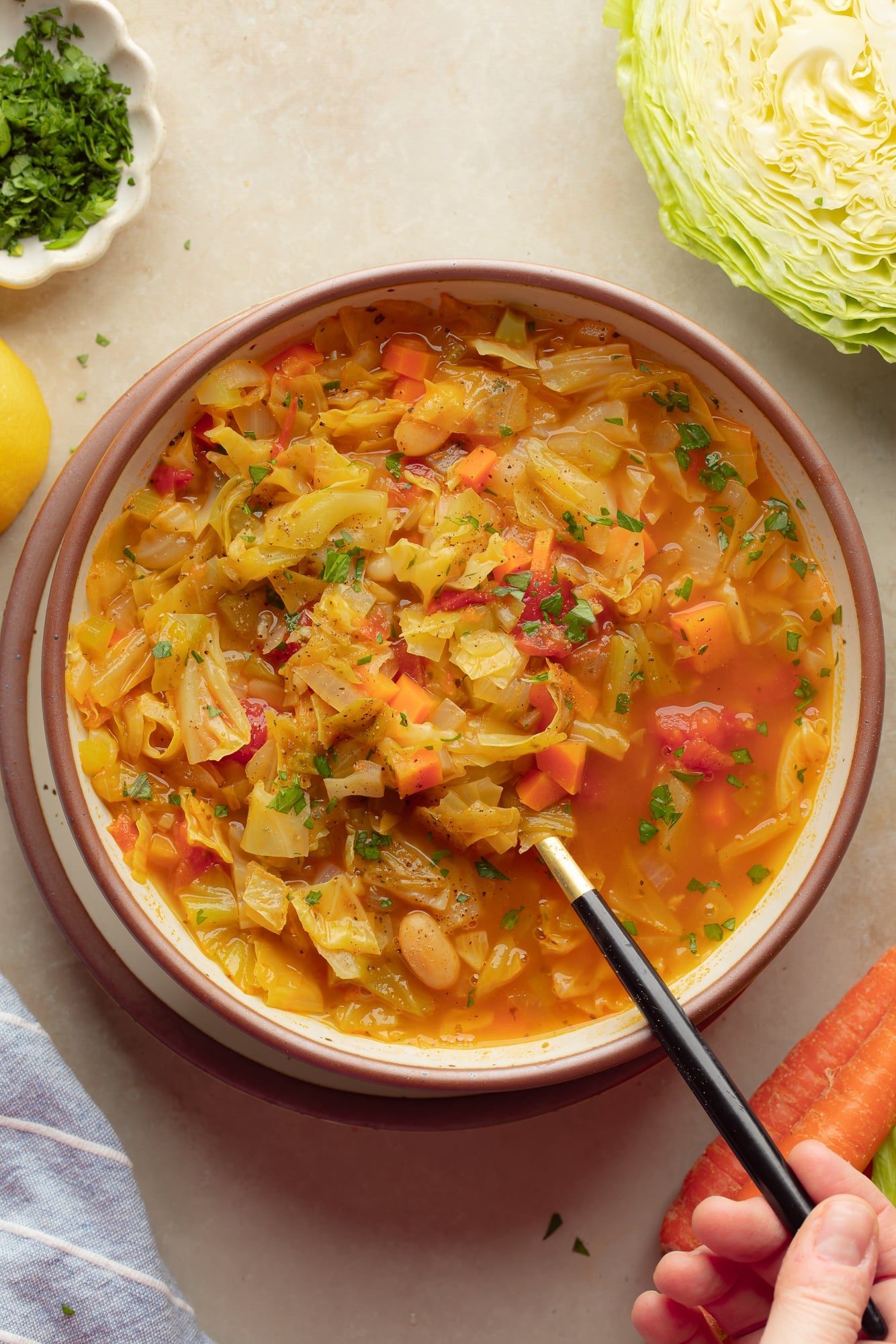 overhead view of a persons hand lifting a spoon out of a bowl of vegan cabbage soup.