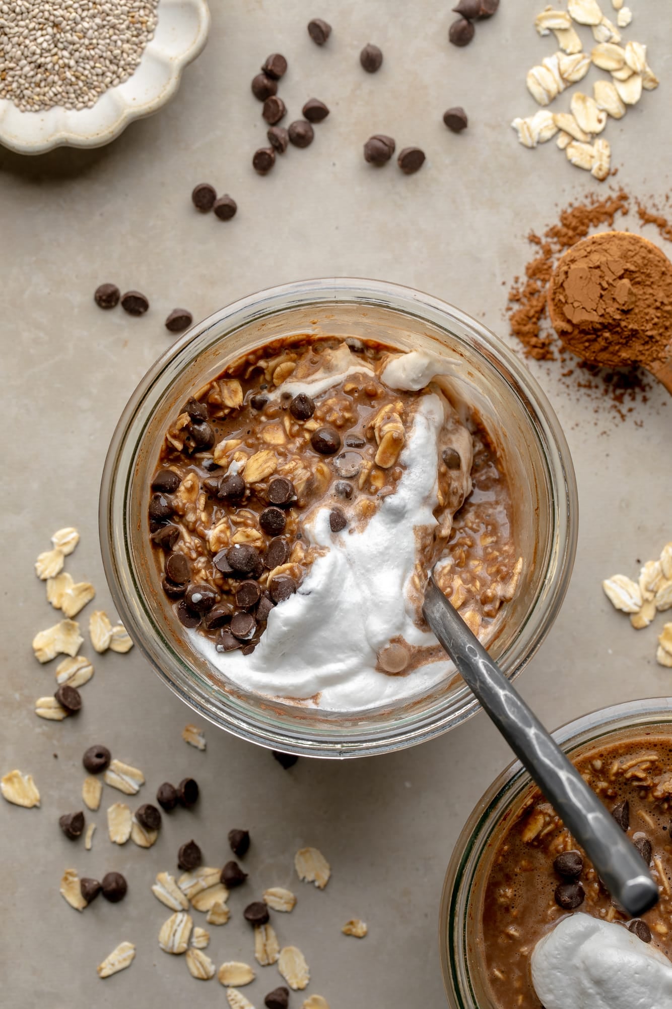 overhead view of a spoon in a jar of chocolate overnight oats topped with vegan whipped cream.