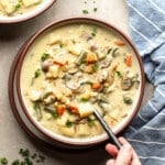 overhead view of a persons hand holding a spoon in a bowl of Creamy Vegetable Soup.