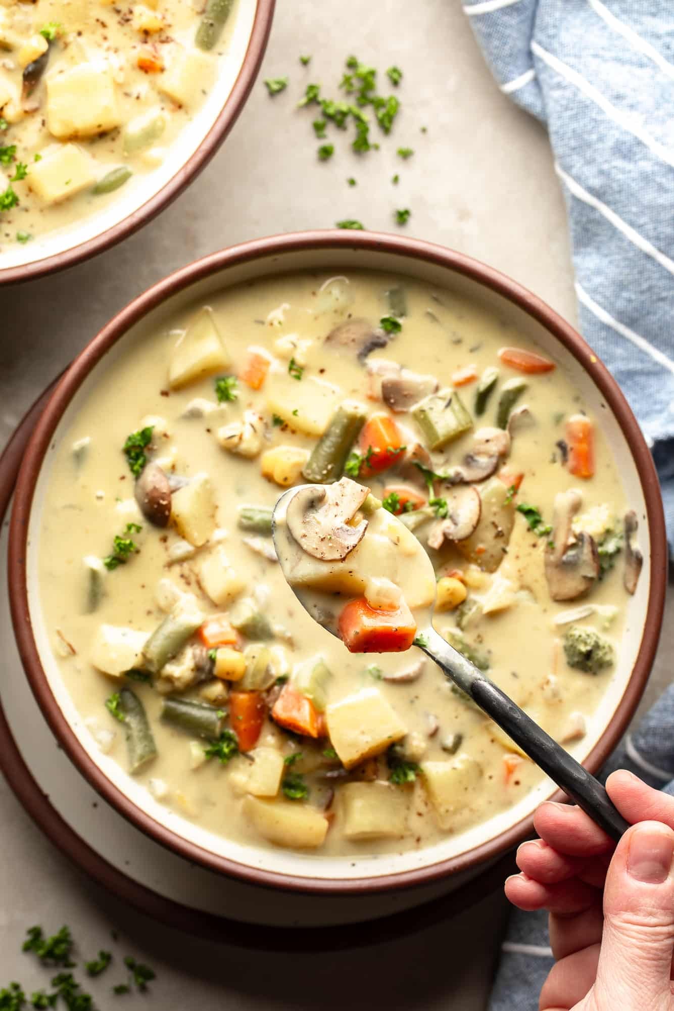 a hand holding a spoon of Creamy Vegetable Soup above a larger bowl of soup.
