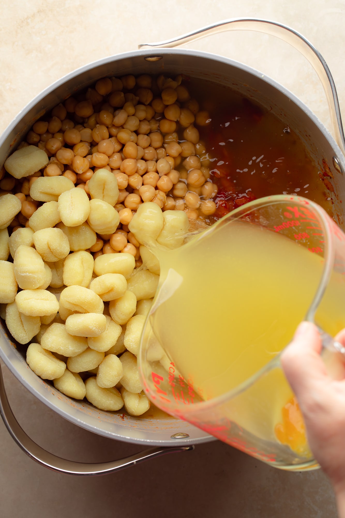 pouring broth into a pot of vegan marry me gnocchi soup.