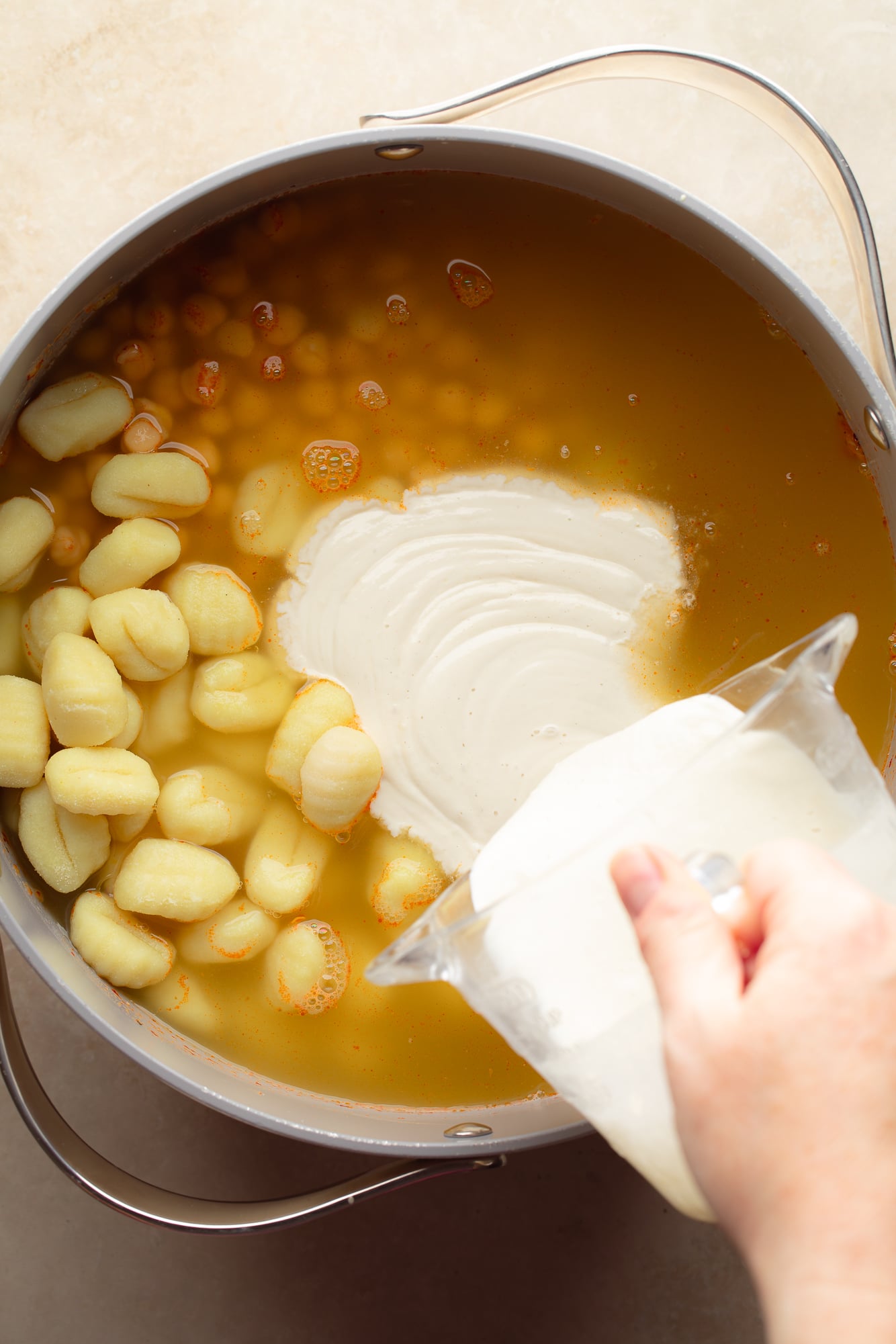 pouring cashew cream into a pot of vegan marry me gnocchi soup.
