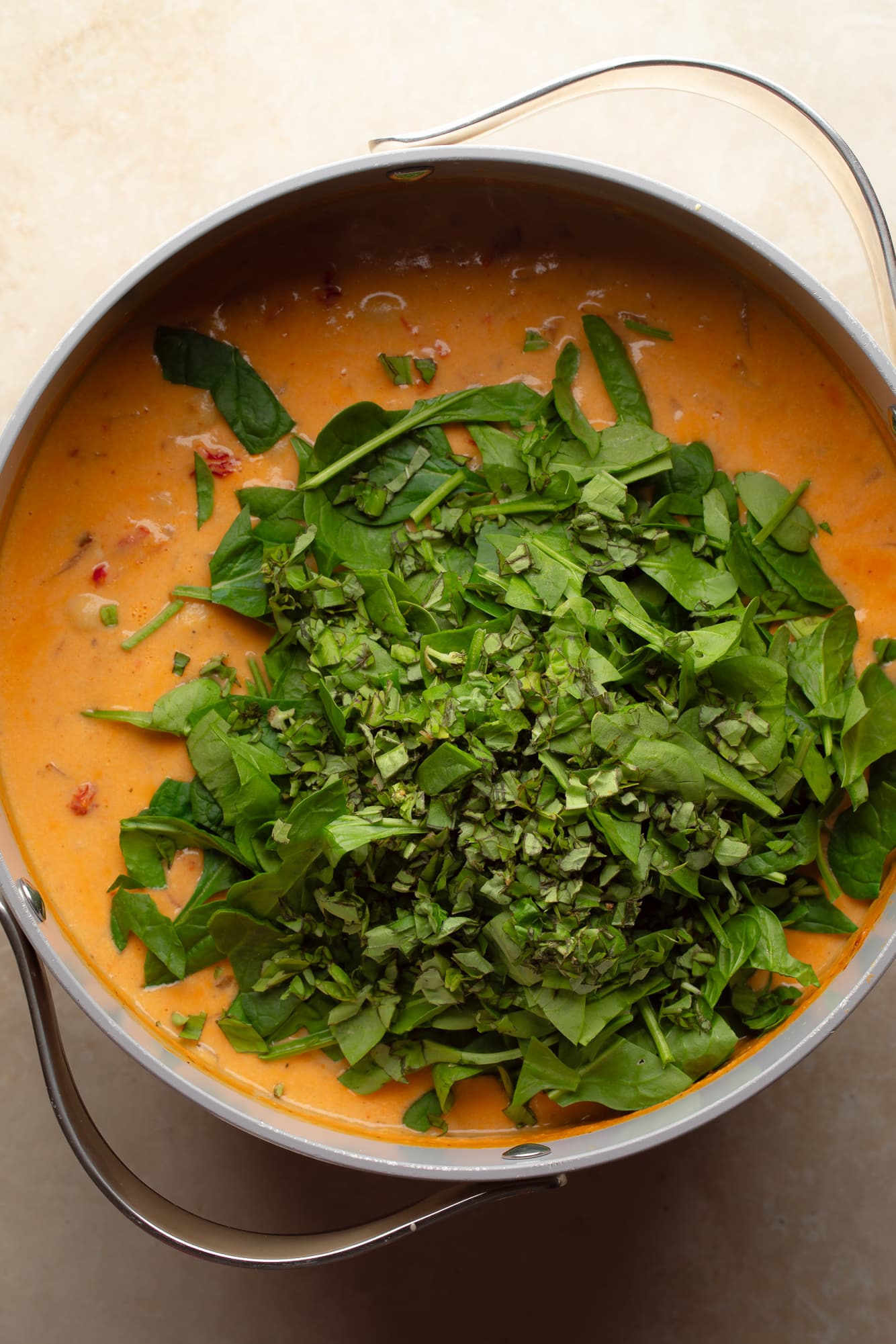 overhead view of a pile of chopped spinach on top of a pot of vegan marry me gnocchi soup.