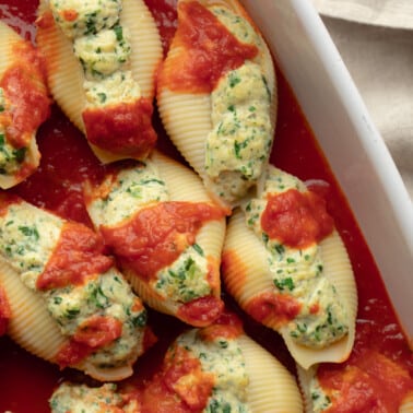 close up on vegan stuffed shells surrounded with marinara sauce in a casserole dish.