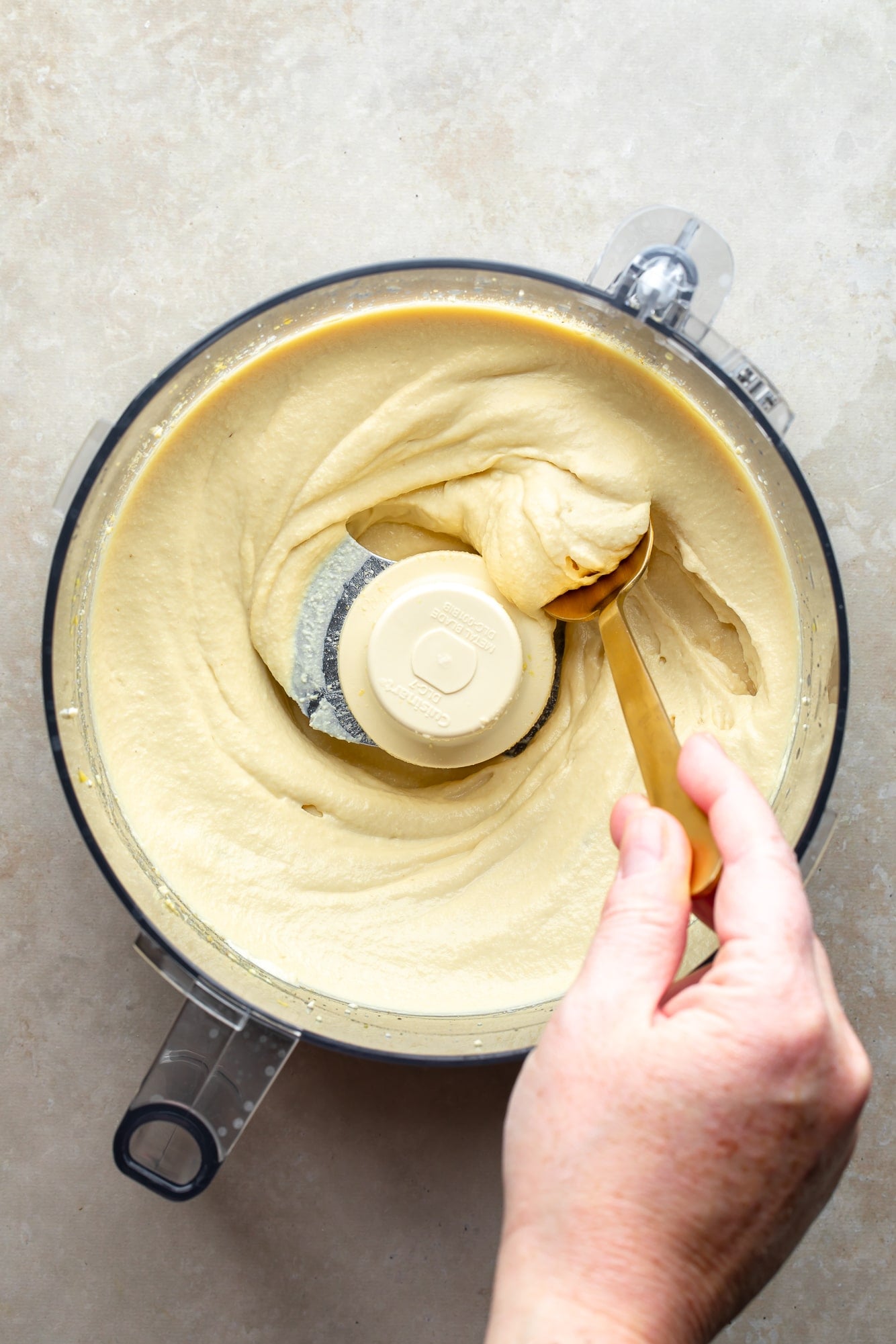 overhead view of a hand running a spoon through a food processer full of whipped tofu ricotta.