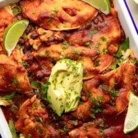 overhead view of a vegan enchilada casserole topped with avocado and lime wedges.