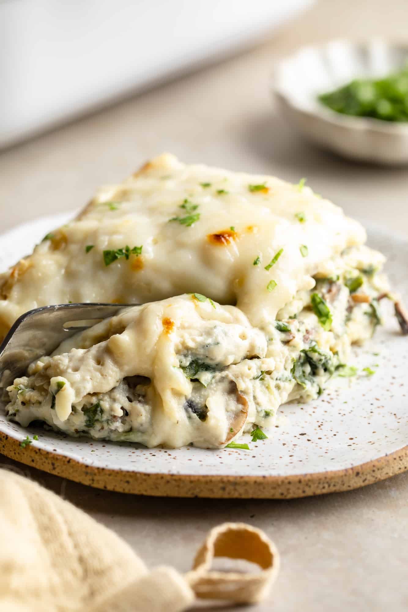 close up on a fork cutting into a slice of vegan white lasagna on a plate.