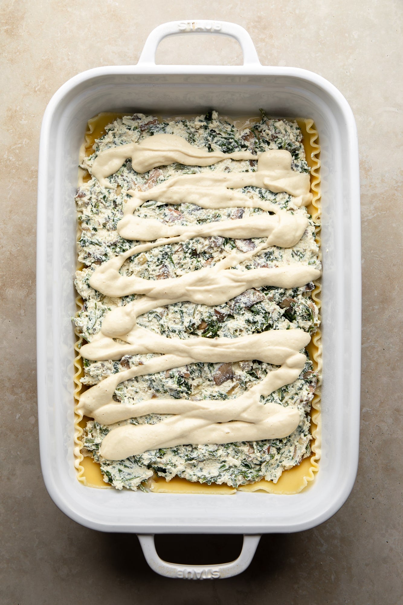 overhead view of assembling a vegan white lasagna in a casserole dish.