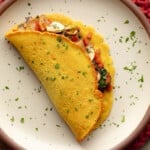 overhead view of a chickpea omelette filled with vegetables on a plate.