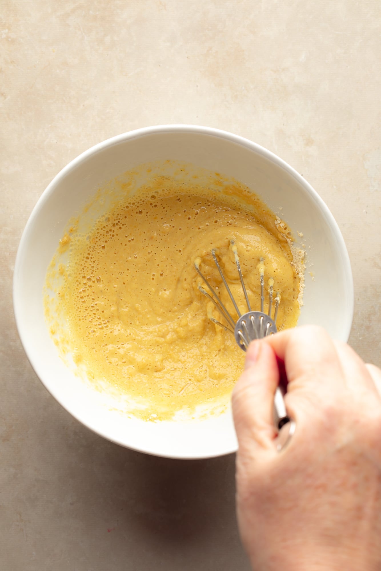 overhead view of a hand whisking the batter for a chickpea flour omelette in a bowl.