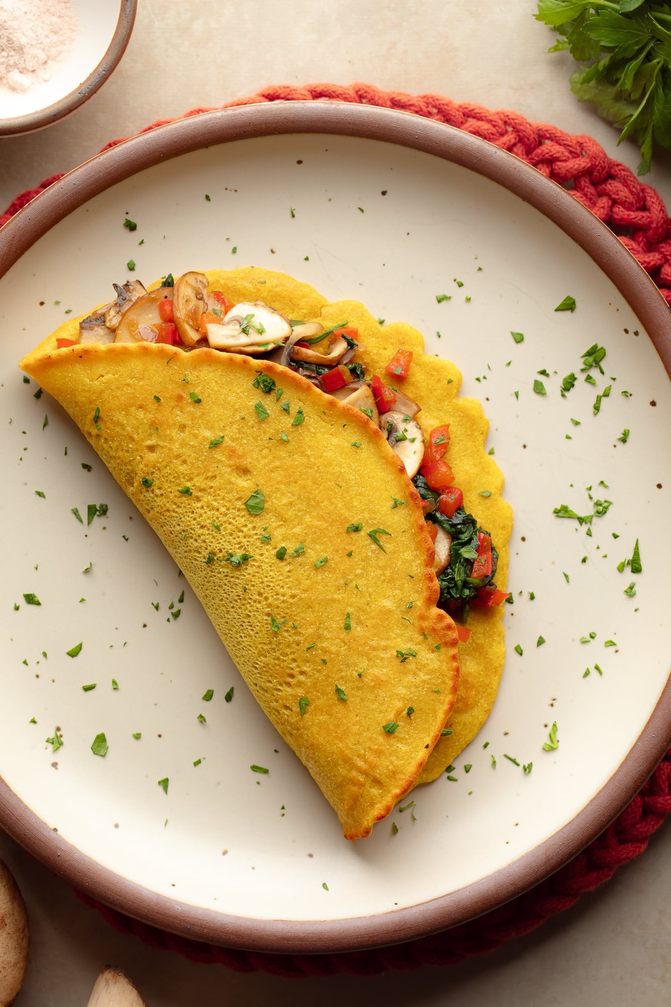 overhead view of a chickpea omelette filled with vegetables on a plate.