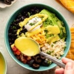 overhead view of a spoon drizzling golden sauce over a comfort rice bowl.