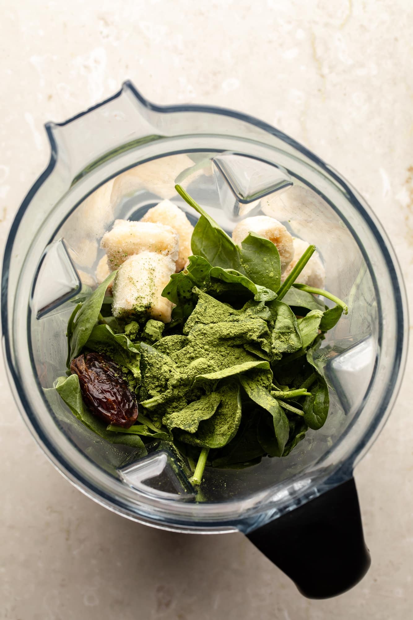 overhead view of the ingredients for a matcha smoothie in a large blender.