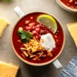 overhead view of a bowl of vegan chili topped with shredded cheese, tomatoes, sour cream, and lime.